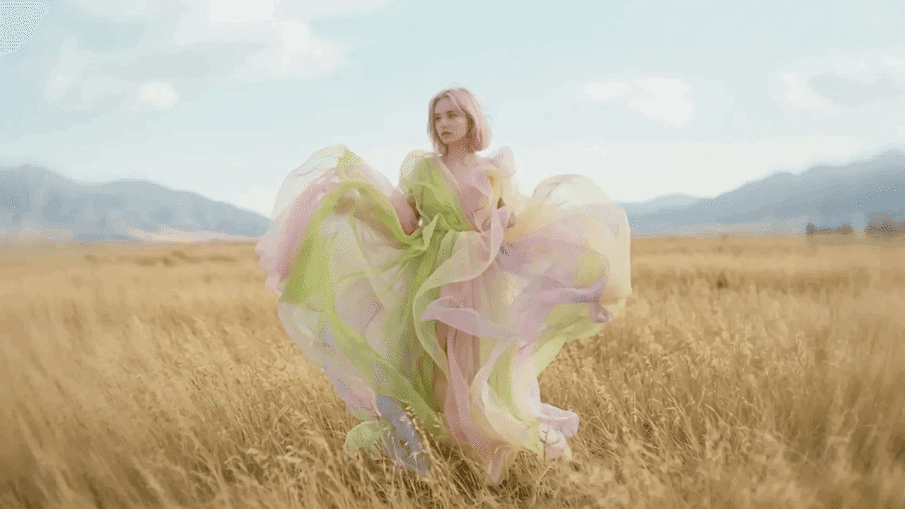Frau in einem fließenden Pastellkleid auf einem goldenen Feld vor Bergen